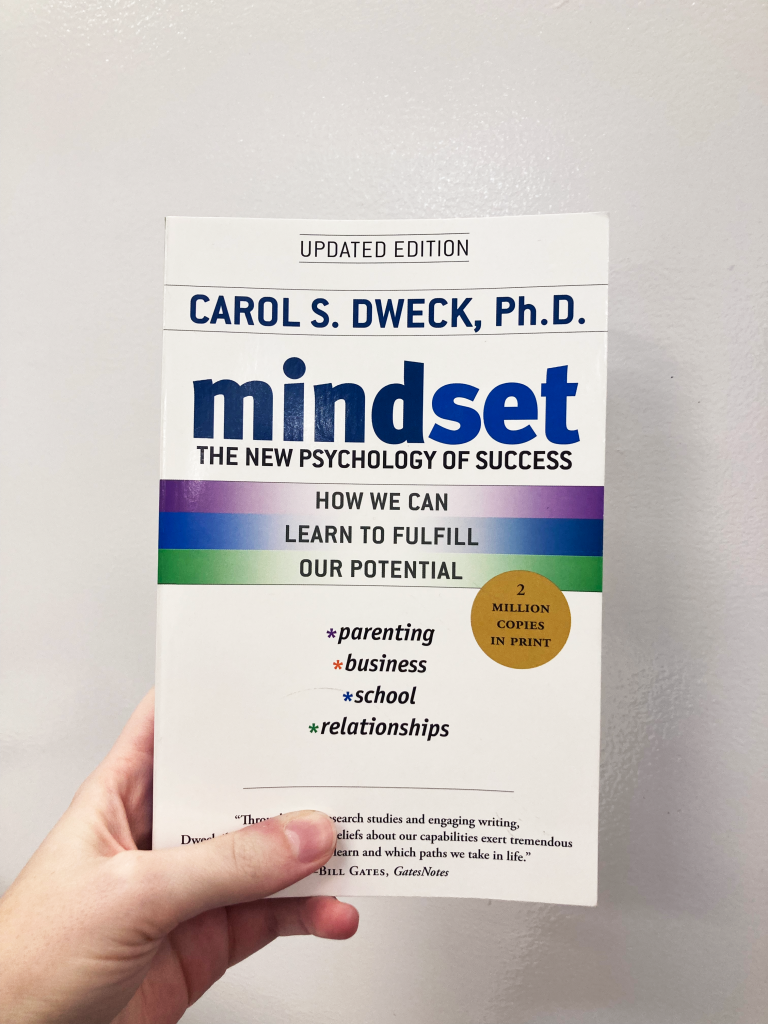 Hand holding white book with blue title: Mindset