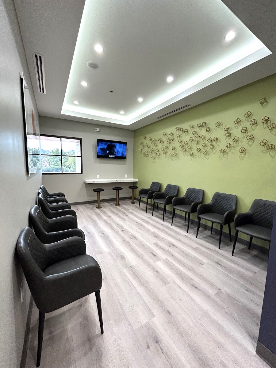 Dental office waiting room with lines of chairs, TV and green accent wall