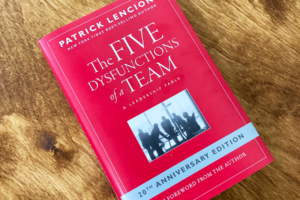 Red book with title "The Five Dysfunctions of a Team" on wooden table