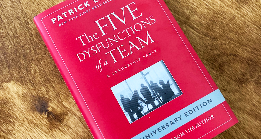 Red book with title "The Five Dysfunctions of a Team" on wooden table